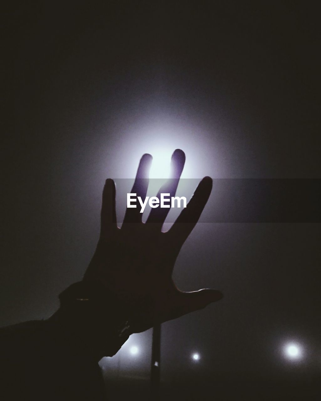 Cropped hand of person against illuminated street light at night