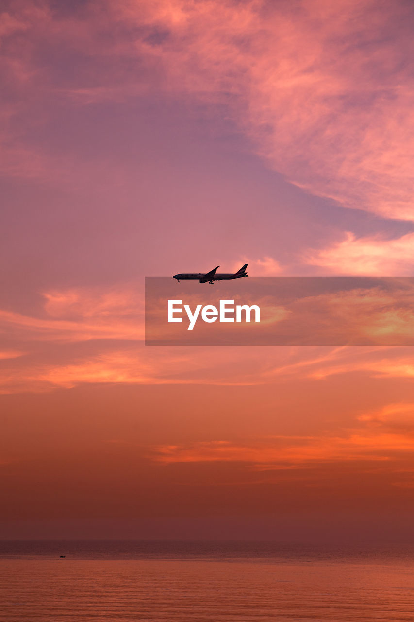 Airplane flying over sea against sky during sunset