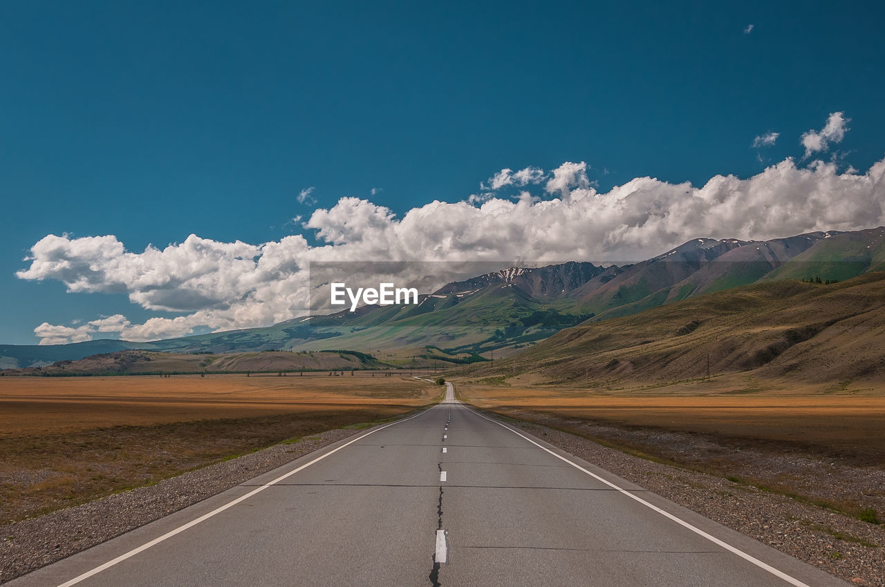 Empty road leading towards mountains against cloudy sky