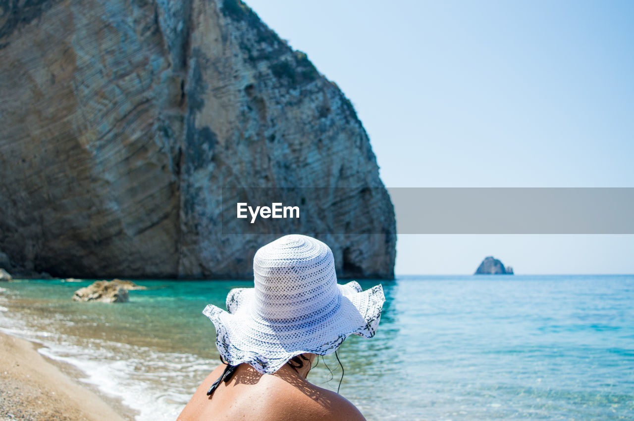 Woman sitting at beach while wearing sun hat on sunny day