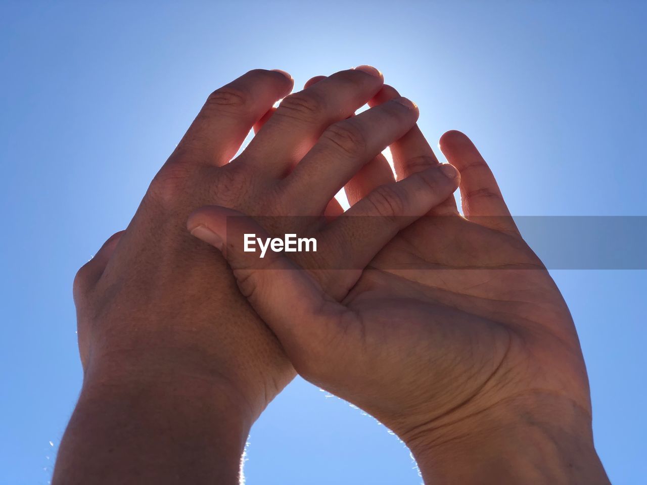 LOW ANGLE VIEW OF HANDS AGAINST BLUE SKY AGAINST CLEAR BACKGROUND