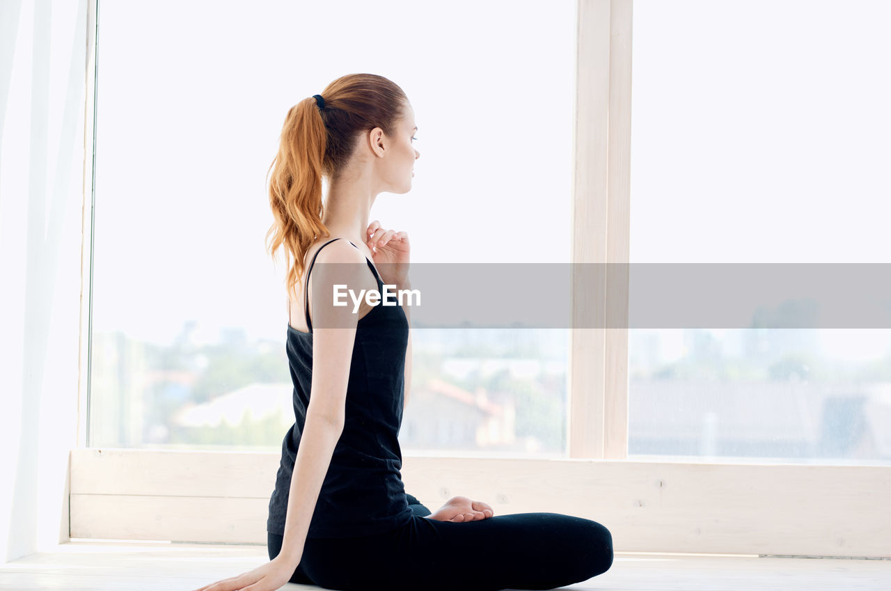 Side view of young woman looking through window