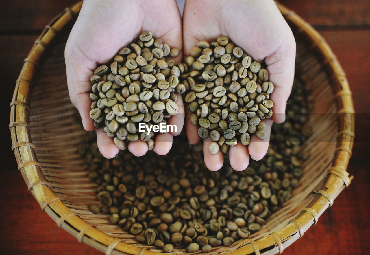 High angle view of hands holding raw coffee beans over basket