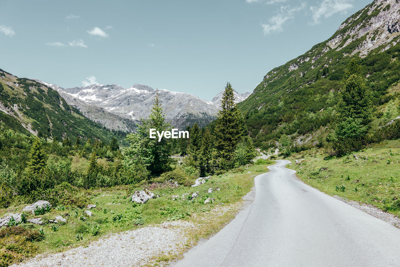 ROAD AMIDST PLANTS AGAINST MOUNTAINS