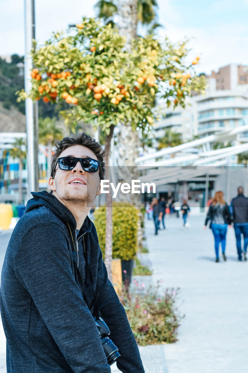 Man in sunglasses looking up while sitting by footpath