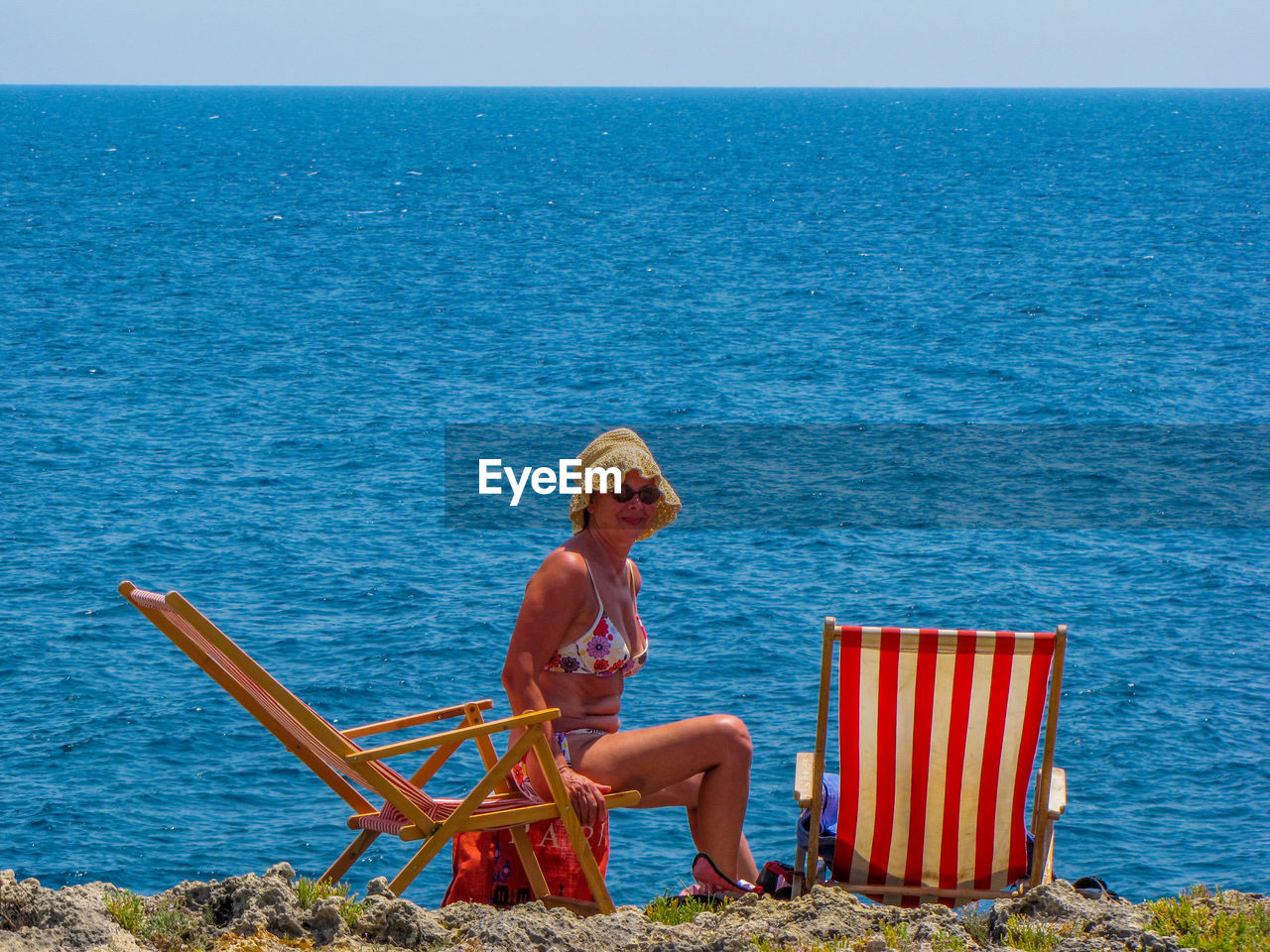 Man sitting on chair by sea against sky