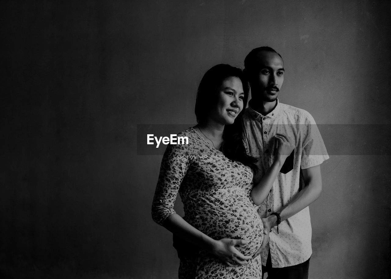 Man with pregnant wife standing against wall