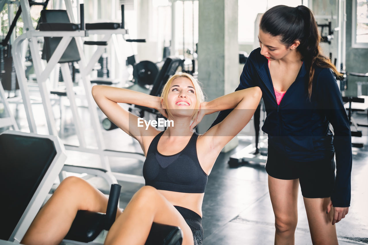 Trainer assisting woman in exercising at gym