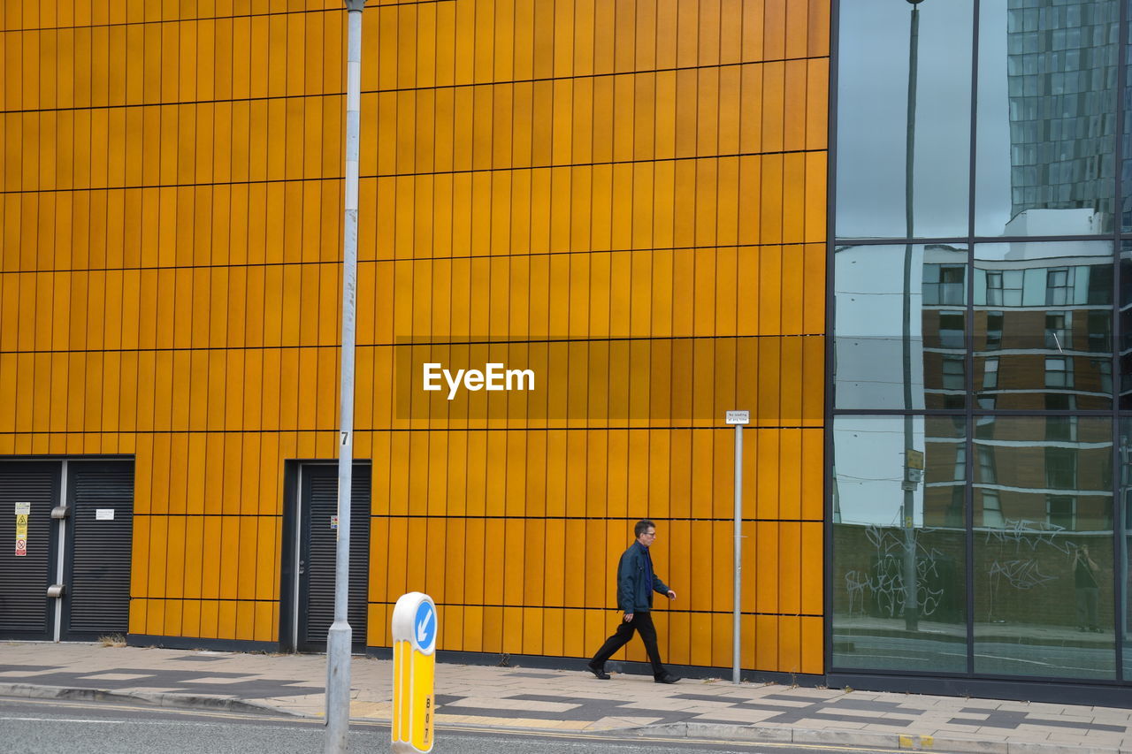 FULL LENGTH REAR VIEW OF MAN WALKING ON YELLOW BUILDING