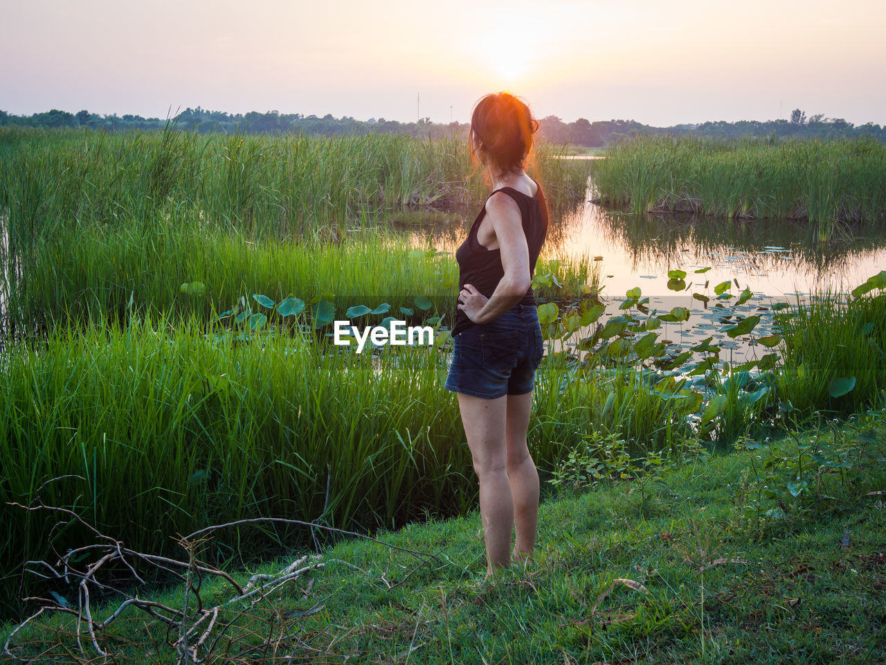 Full length of woman standing by lake during sunset