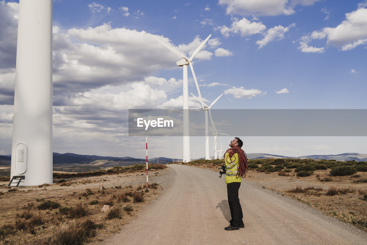 Technician with rope standing on road looking at wind turbine