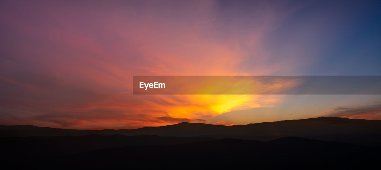 SCENIC VIEW OF SILHOUETTE MOUNTAINS AGAINST DRAMATIC SKY