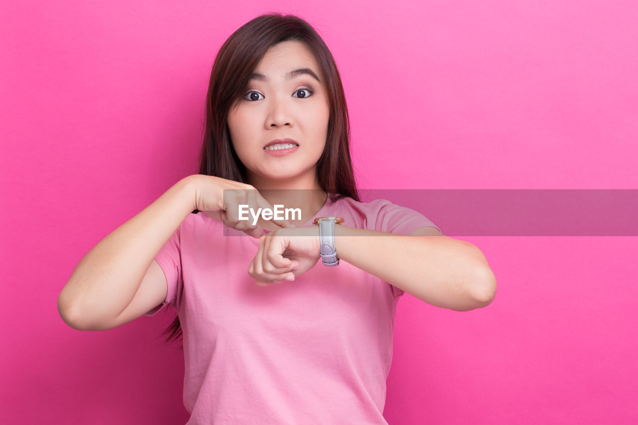 PORTRAIT OF BEAUTIFUL YOUNG WOMAN STANDING AGAINST PINK BACKGROUND