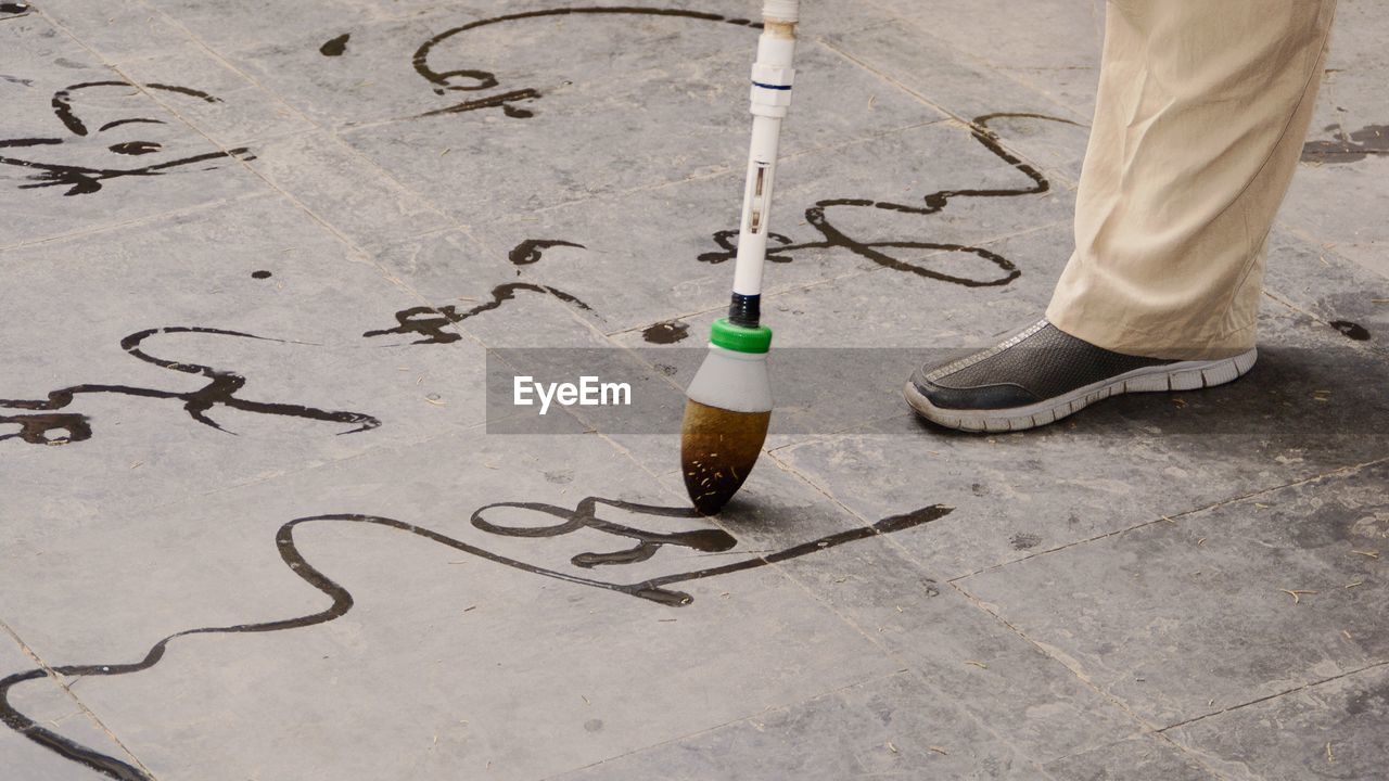 Low section of man practicing calligraphy with water brush on street