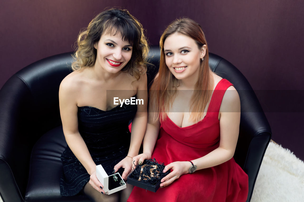 Portrait of smiling women holding gift box while sitting on sofa