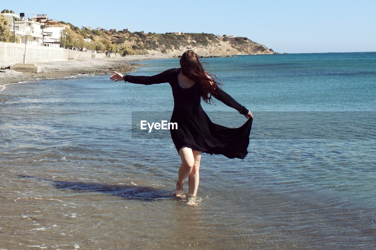 Young woman standing on beach against clear sky