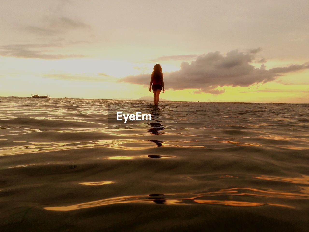 Rear view of woman standing in water at beach against sky during sunset