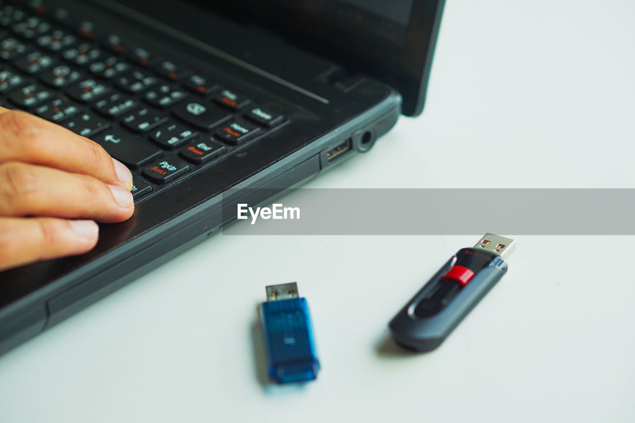 Cropped hand using laptop by usb sticks on table