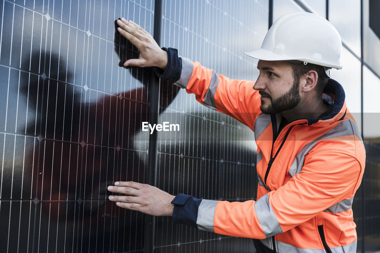 Focused engineer wearing hardhat examining solar panels