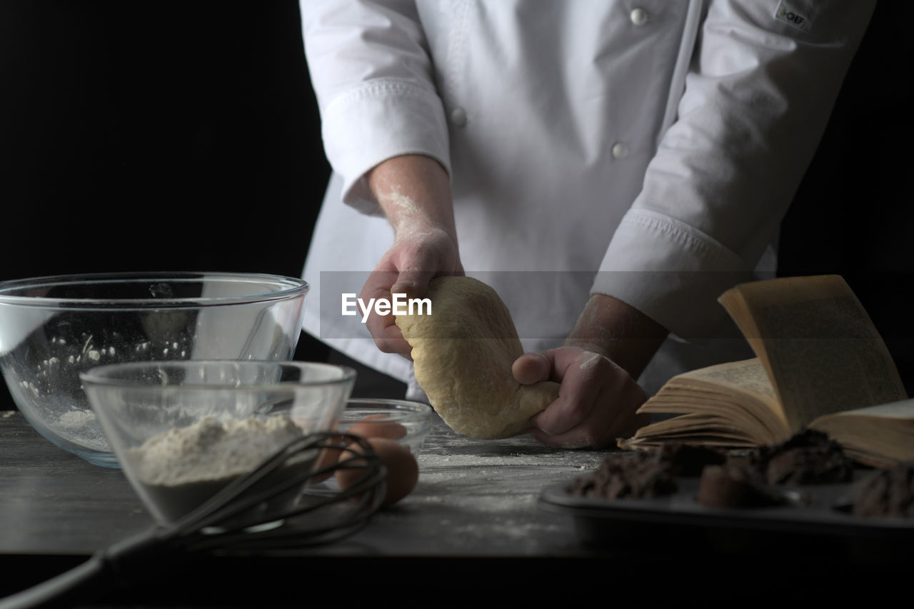 Midsection of chef kneading dough against black background