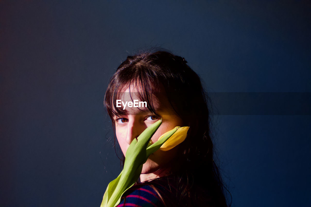 Portrait of woman holding flower against blue background