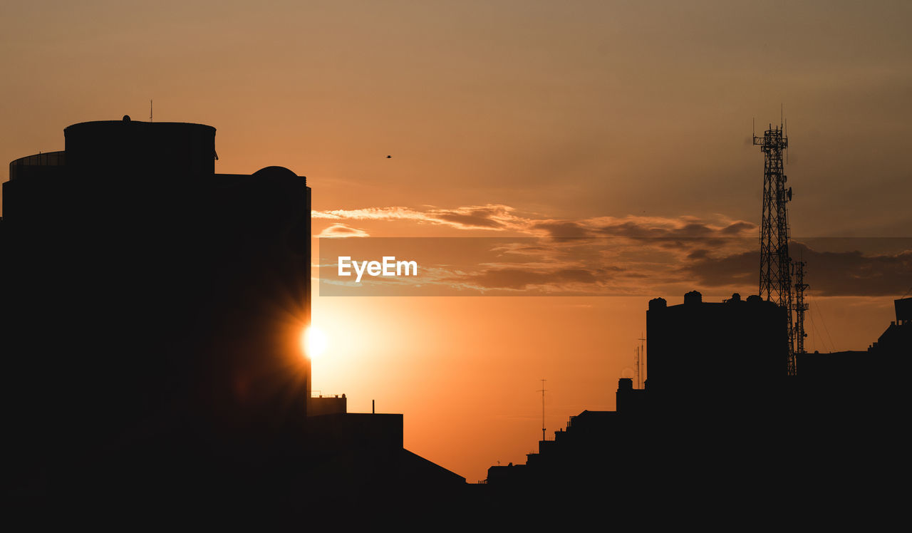 SILHOUETTE BUILDINGS AGAINST ORANGE SKY DURING SUNSET