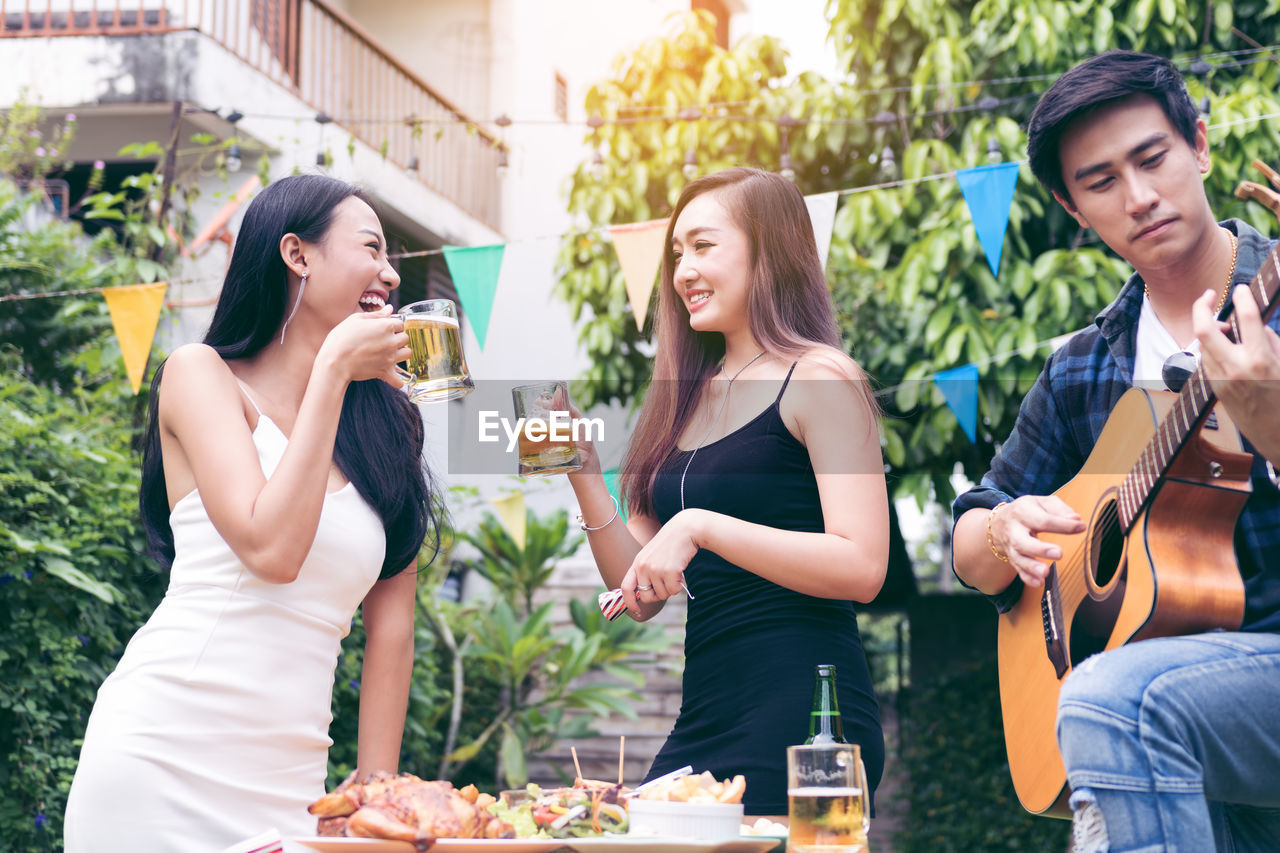 Man playing guitar by female friends enjoying beer