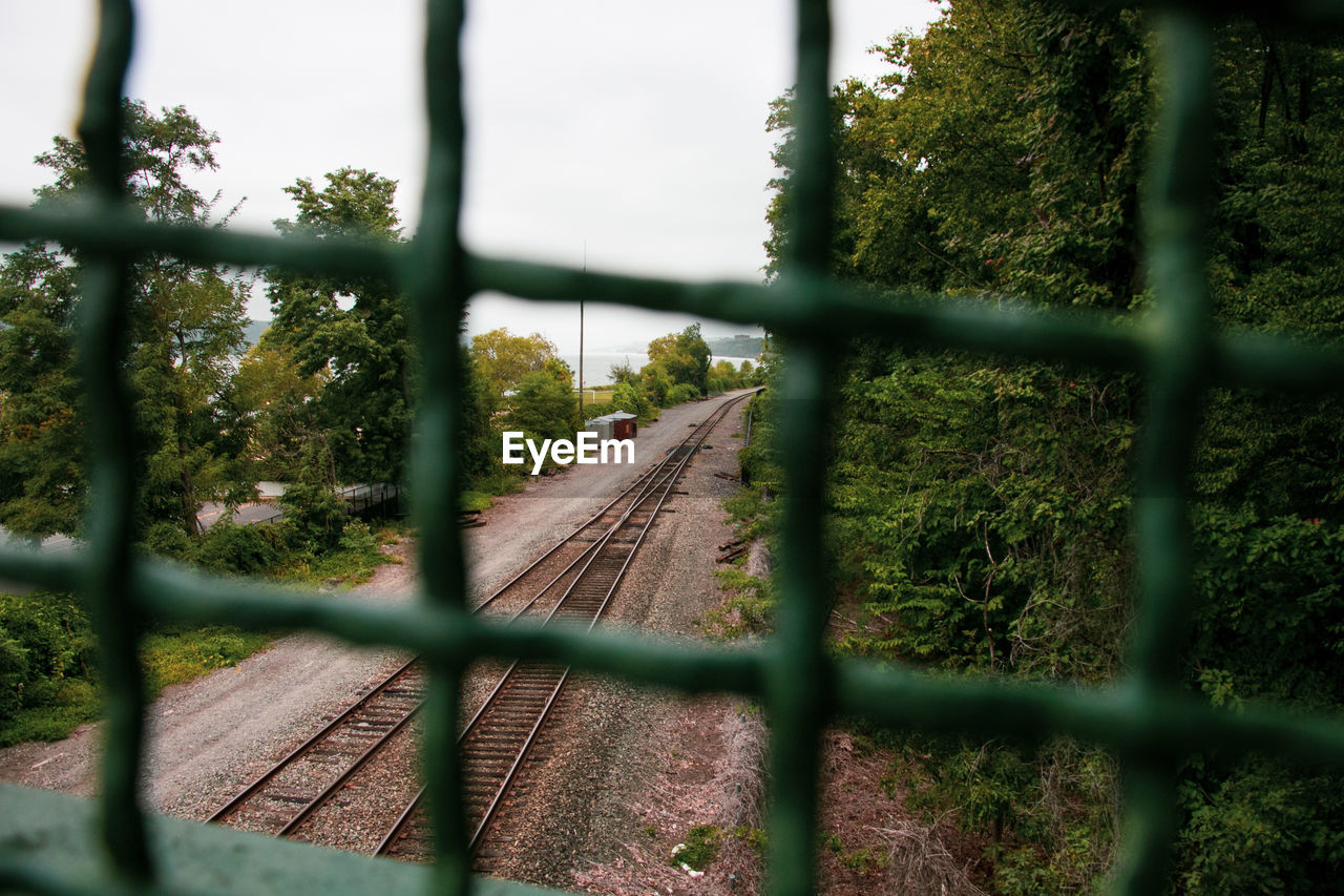 An active train track surrounded by local greenery, framed by a fence