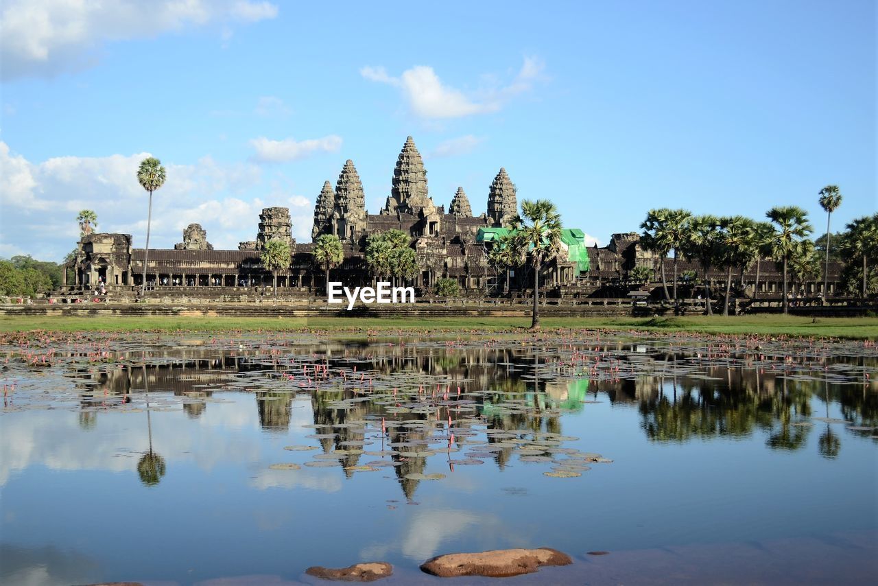 Angkor wat temple by lake against blue sky