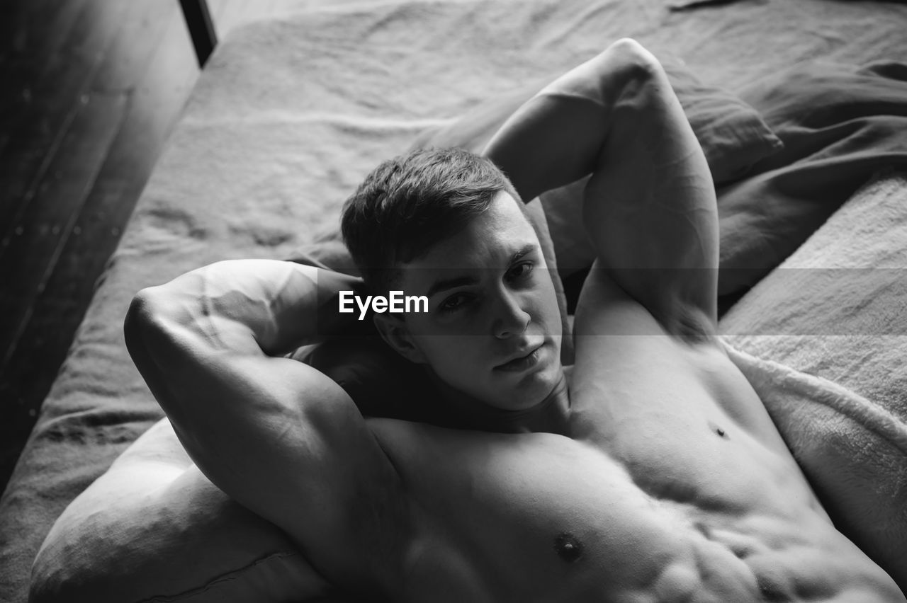 High angle portrait of shirtless man lying on bed at home