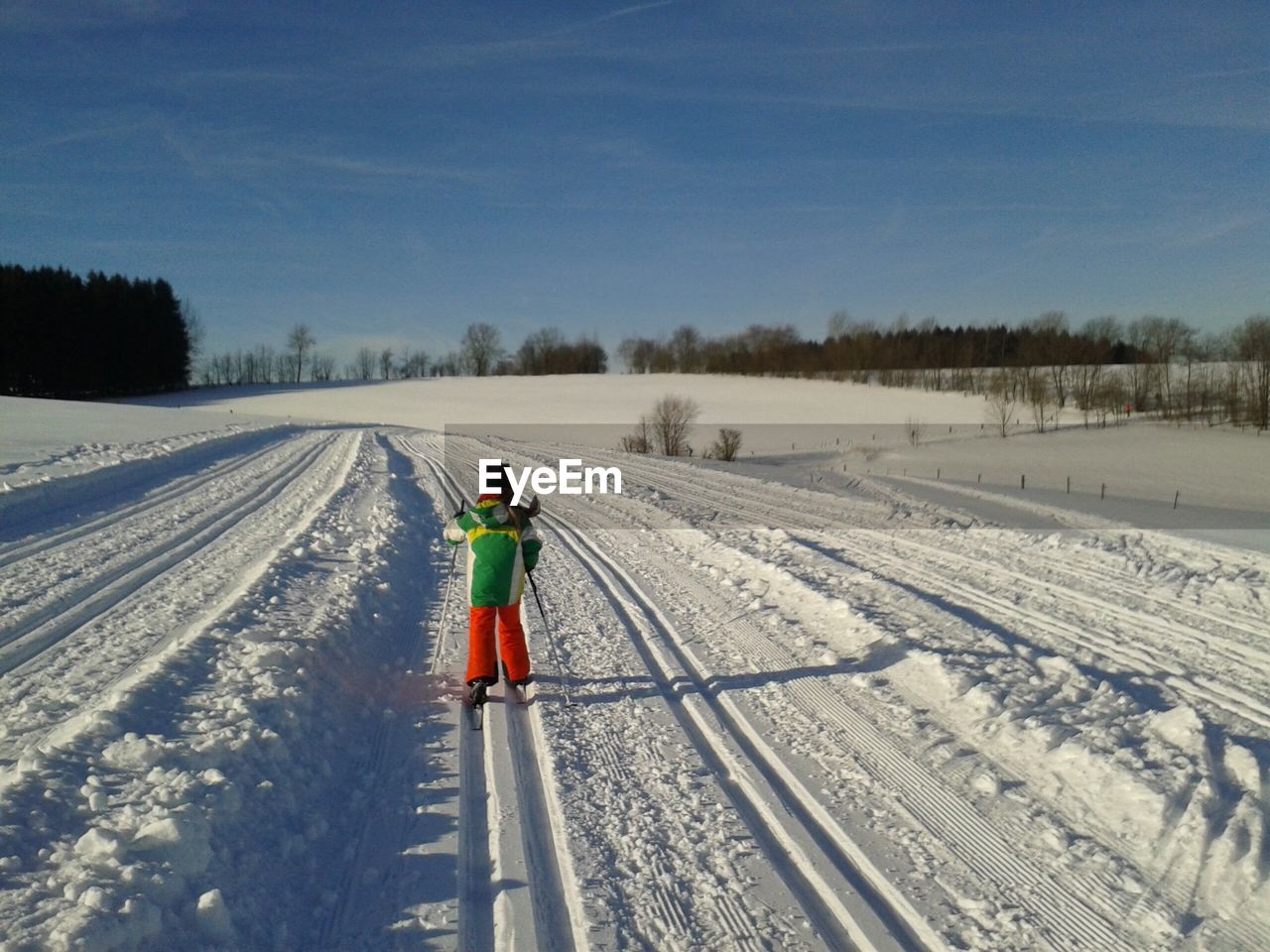 REAR VIEW OF MAN WALKING ON SNOW COVERED FIELD AGAINST SKY