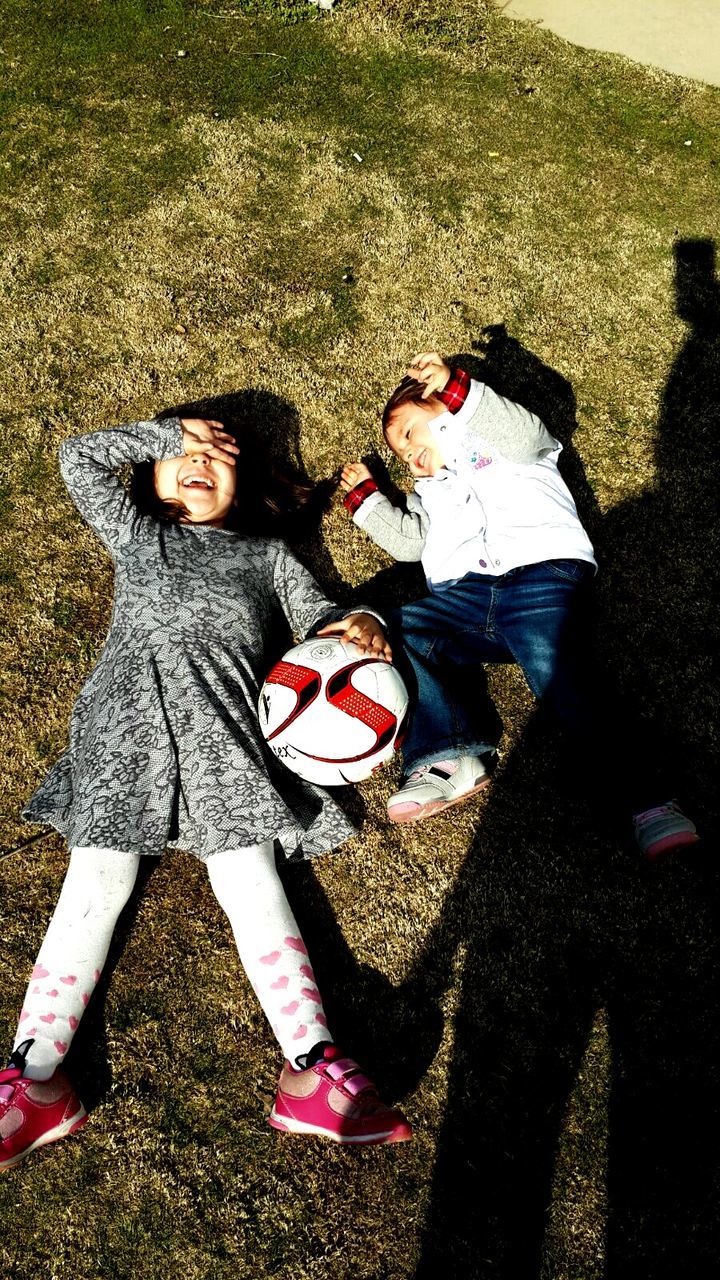 High angle view of happy sibling lying on grassy field