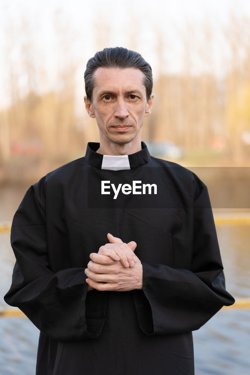 Portrait of priest standing against trees