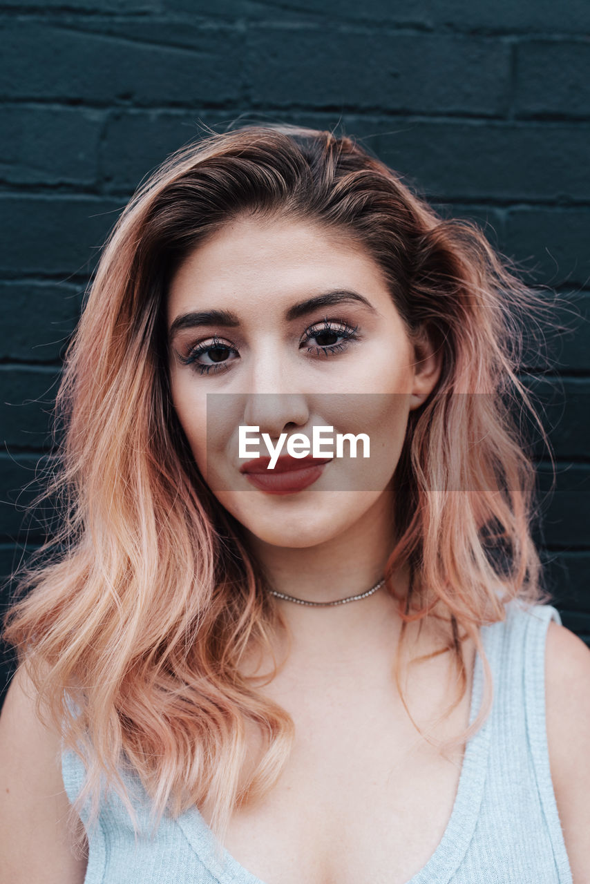 Portrait of beautiful woman with dyed hair against black brick wall