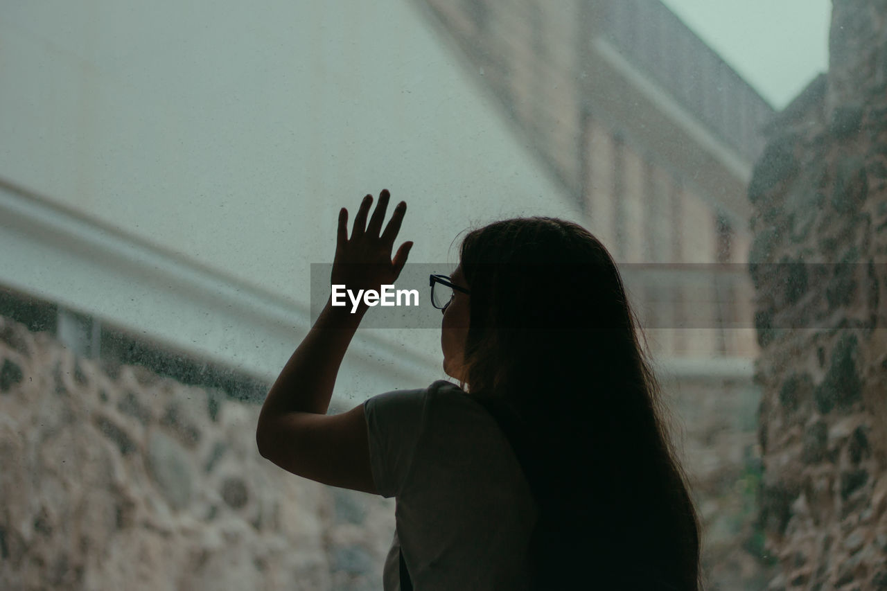 Rear view of woman touching wet window during rainy season