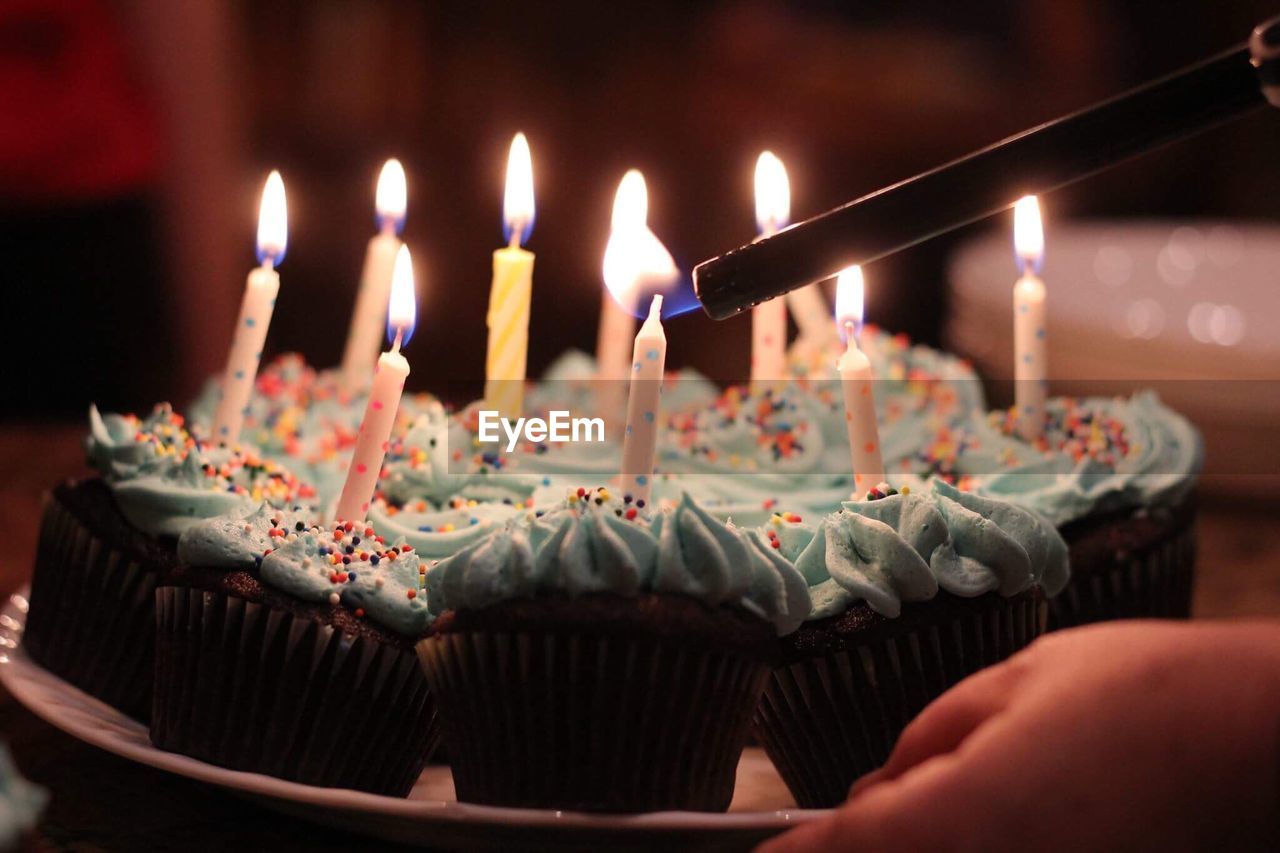 Cropped hand igniting birthday candles on cupcakes in darkroom