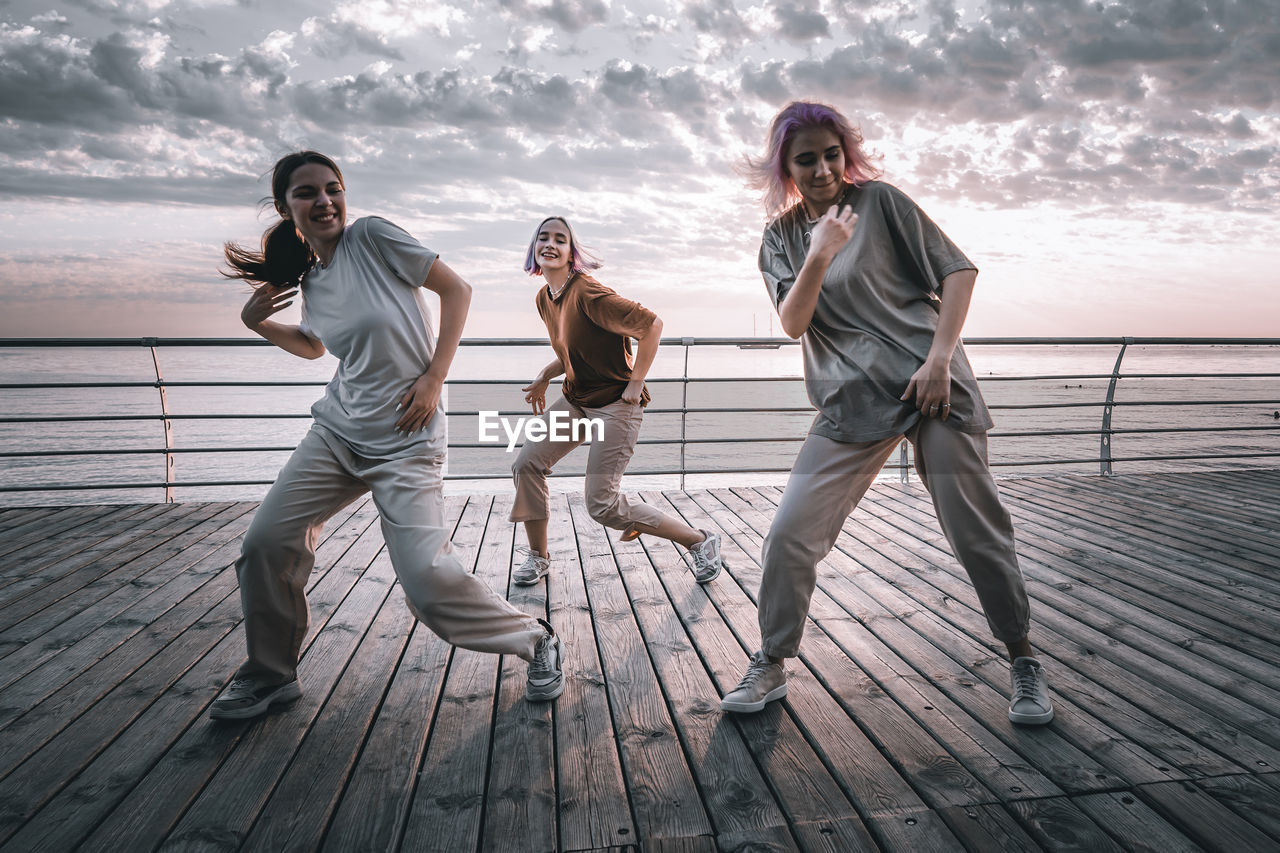 Full length of smiling women dancing against sea and sky