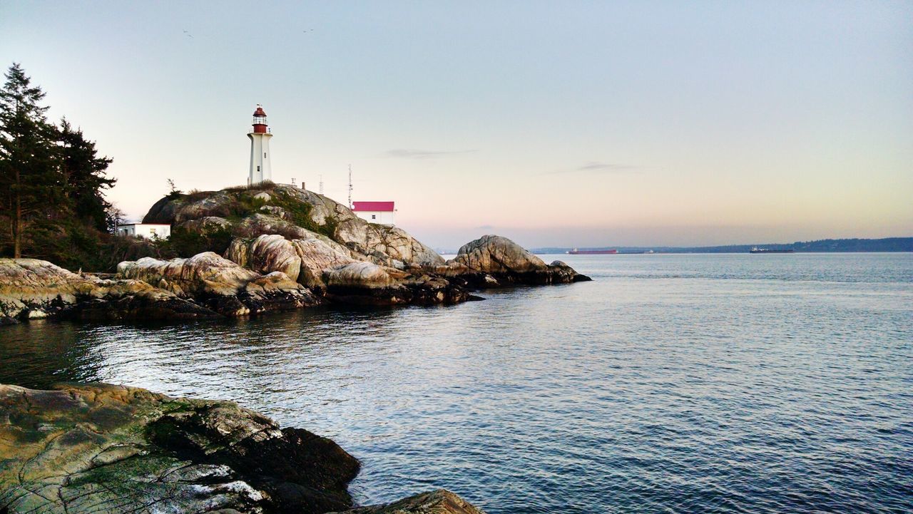 Lighthouse on rock by sea against sky at sunset