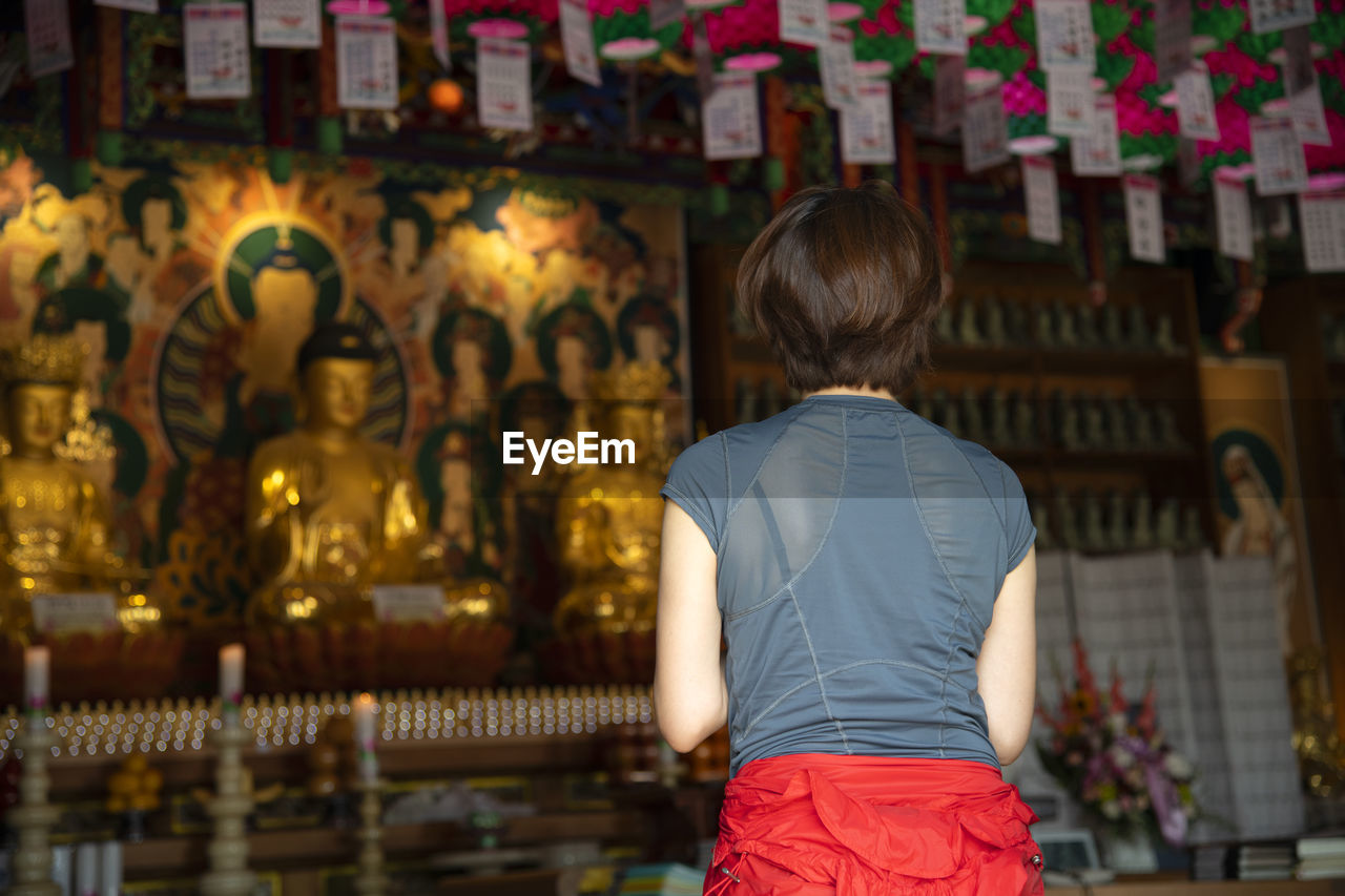 REAR VIEW OF WOMAN WITH STATUE AGAINST TEMPLE