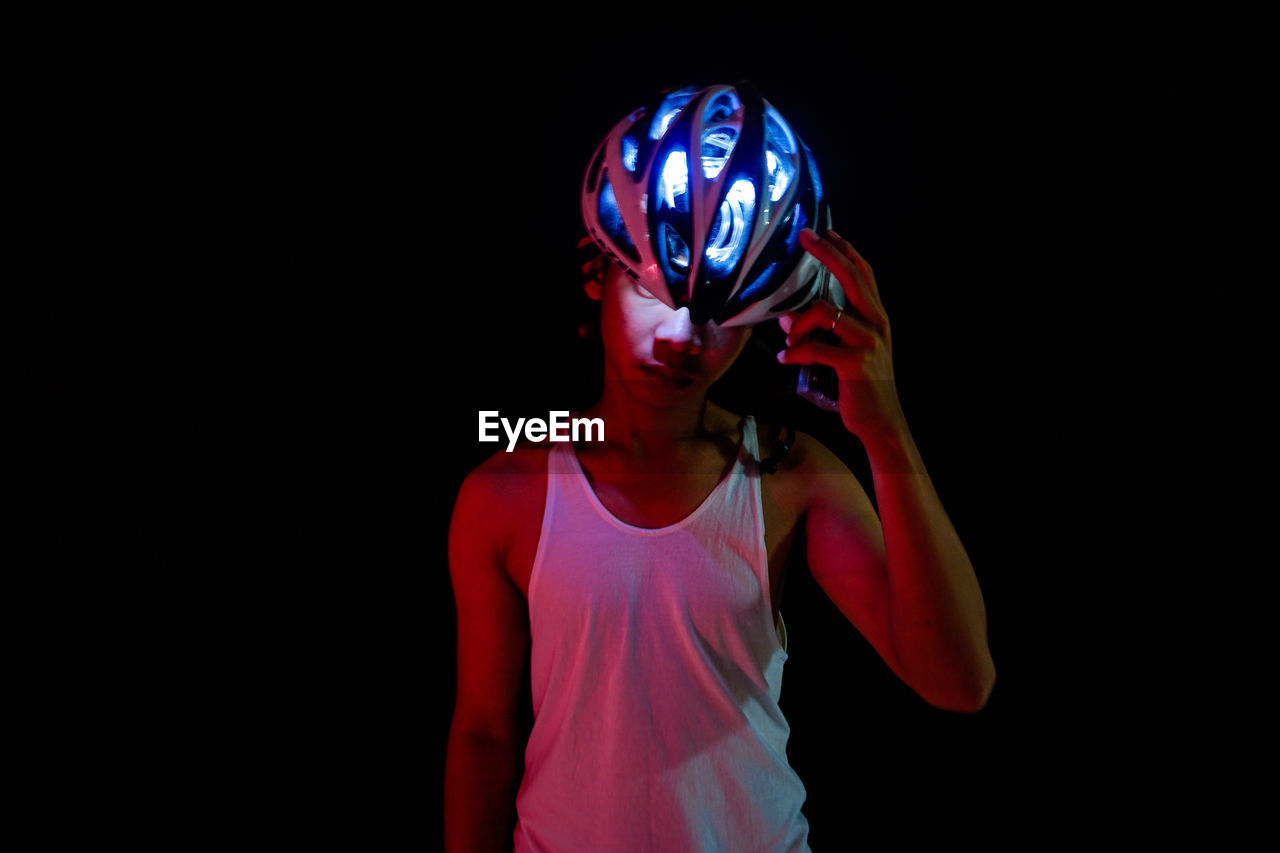 Man holding illuminated cycling helmet in darkroom