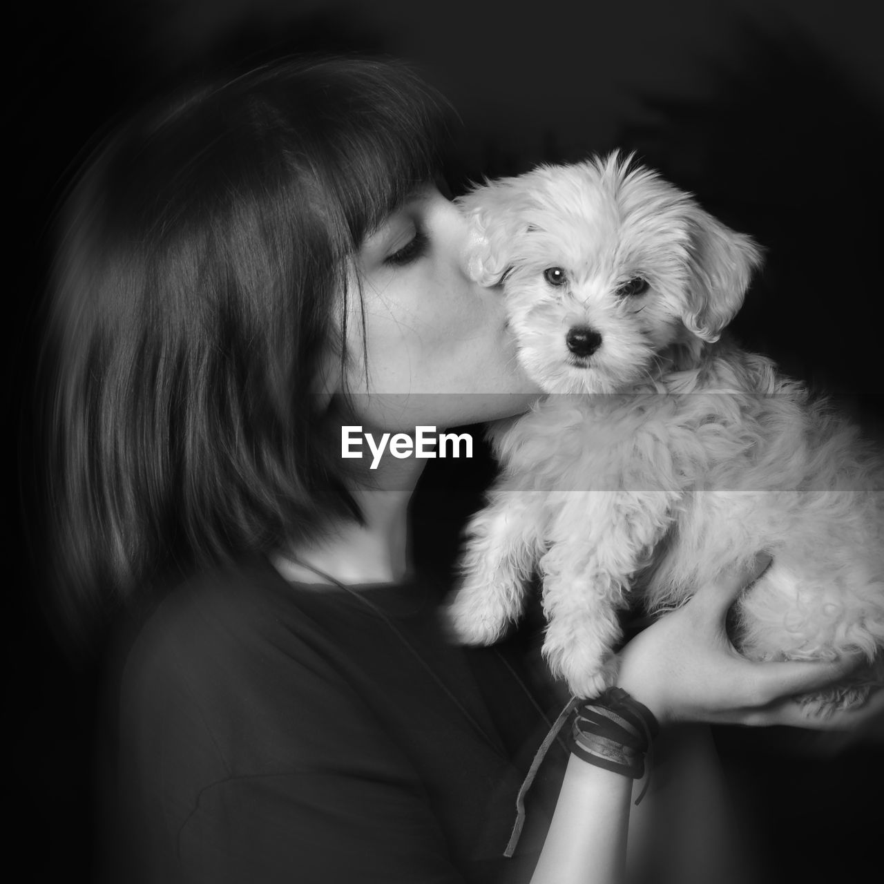 Woman kissing puppy against black background