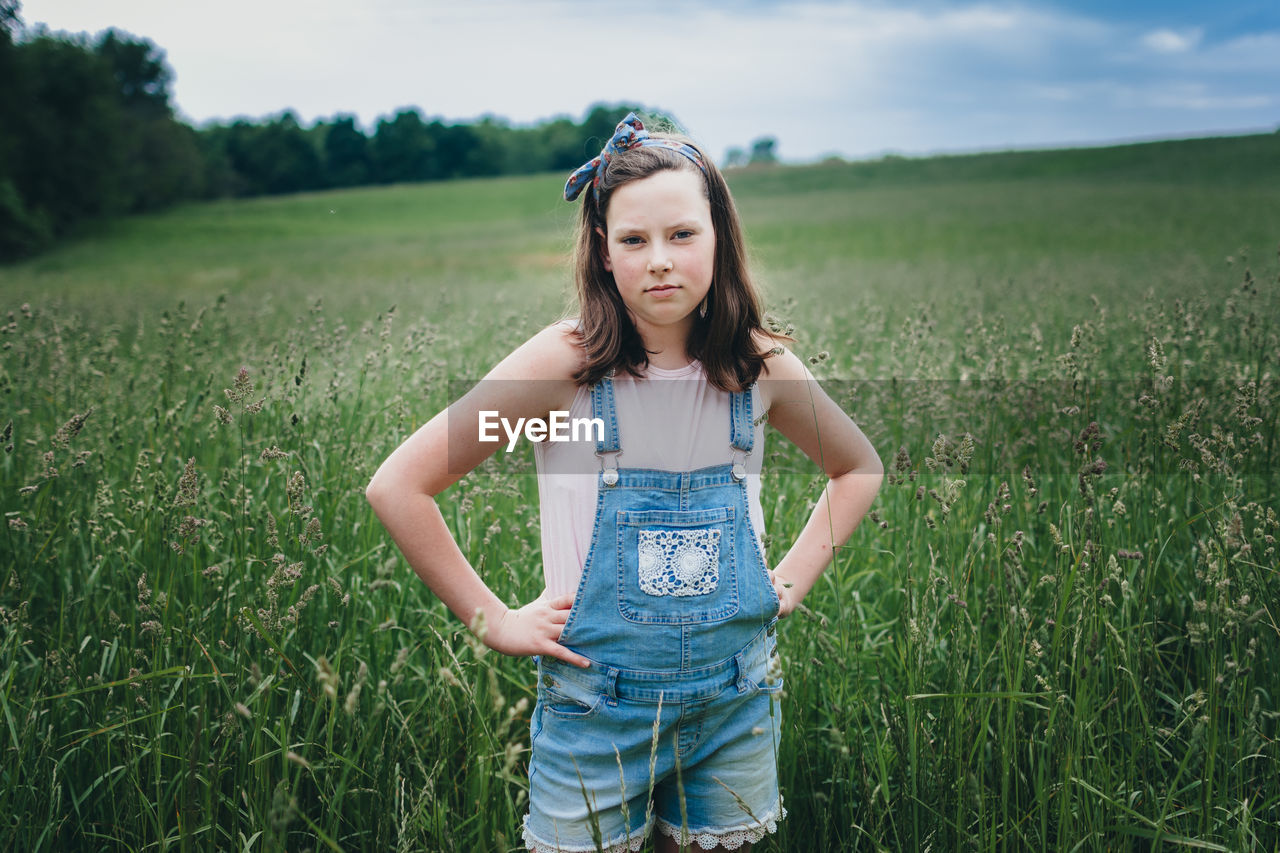 Teen girl in overall shorts standing in grassy field in the midwest