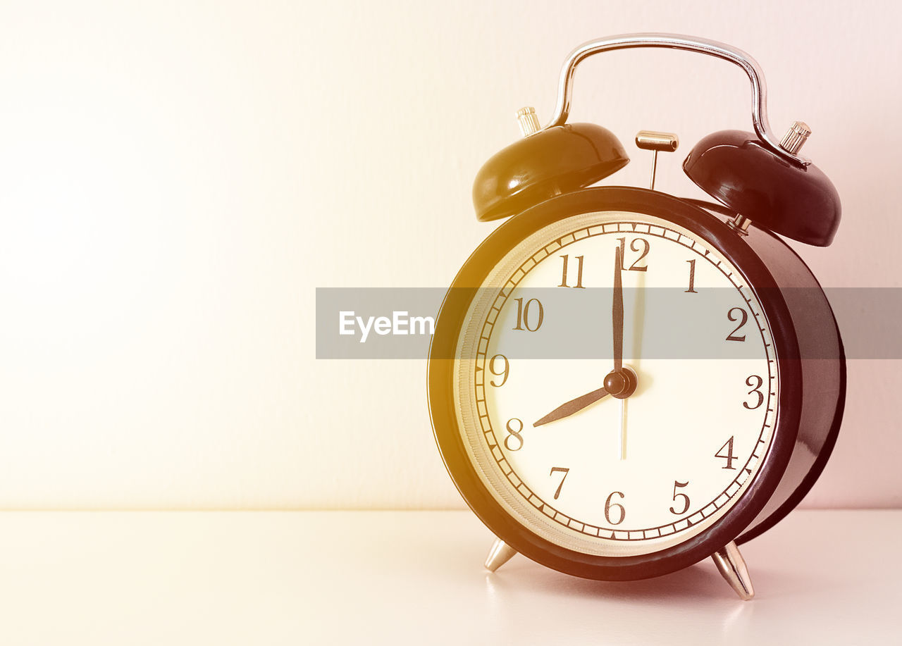 CLOSE-UP OF CLOCK ON TABLE AGAINST WHITE BACKGROUND