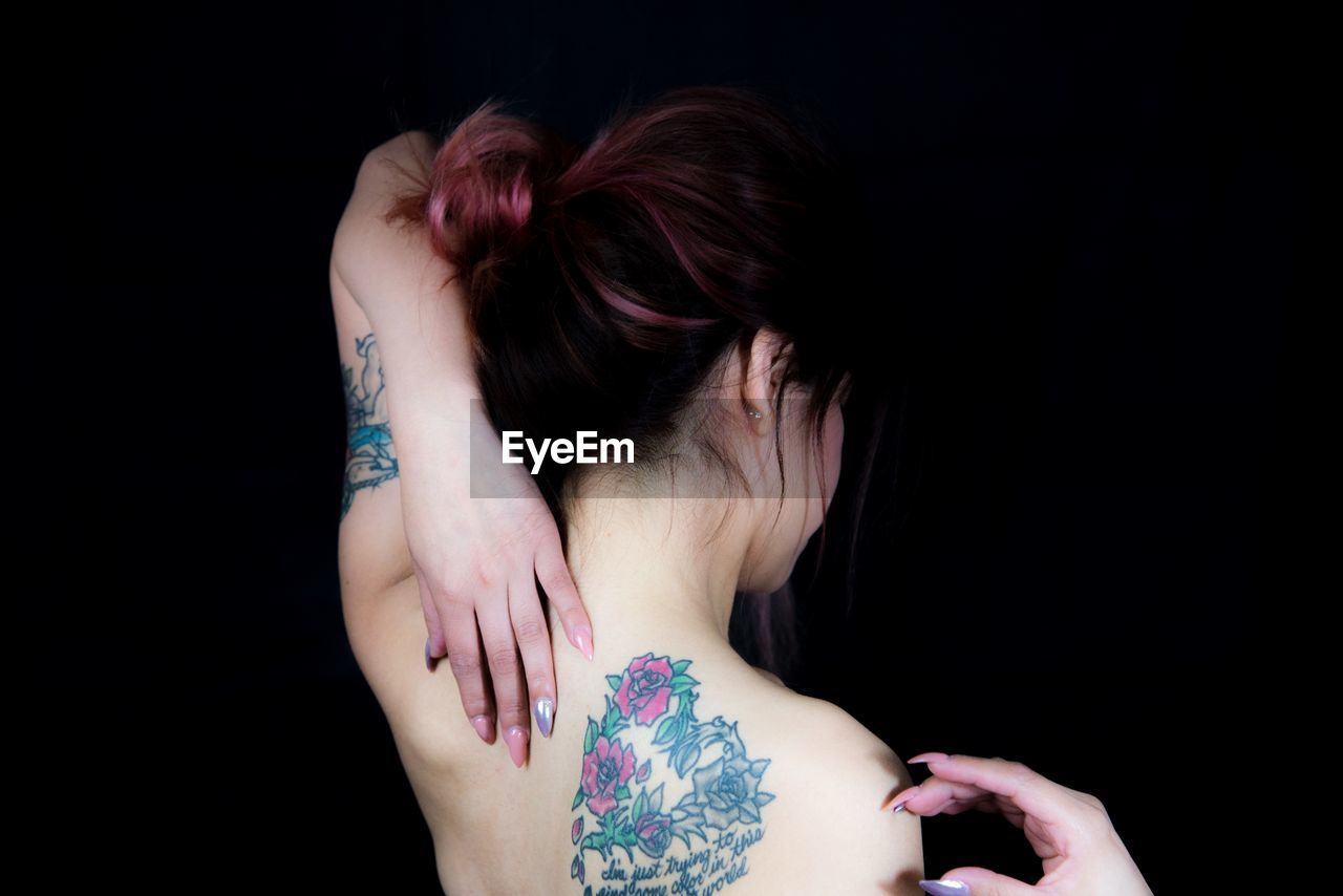 Shirtless woman with tattoo against black background