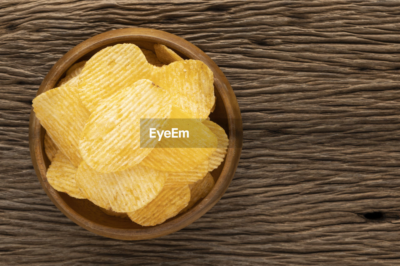 Tasty ridged potato chips in wooden bowl on rustic natural wood with copy space for text, top view