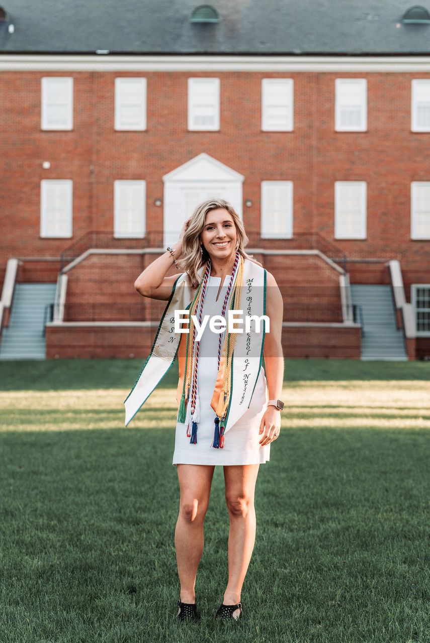 PORTRAIT OF SMILING YOUNG WOMAN STANDING AGAINST BUILDING