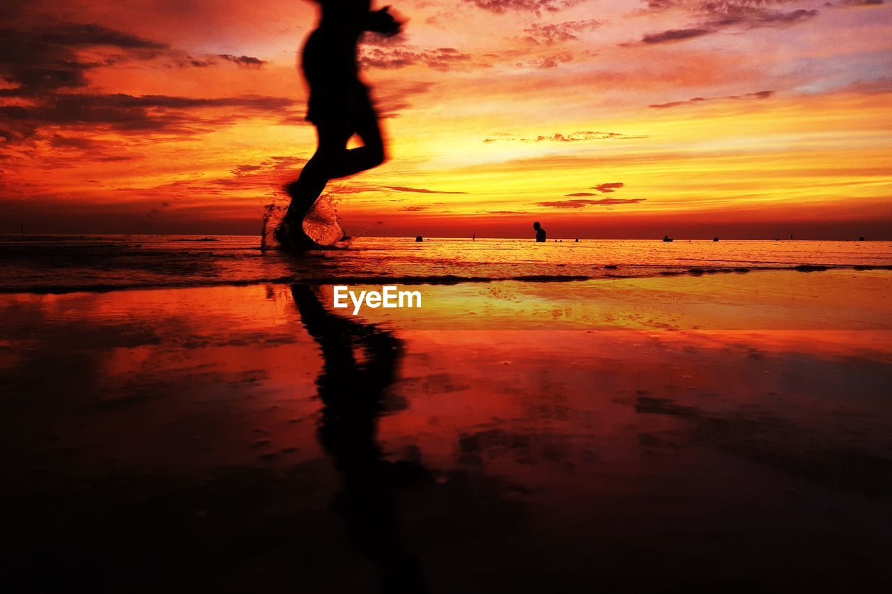 Low section of person running on shore against sea during sunset