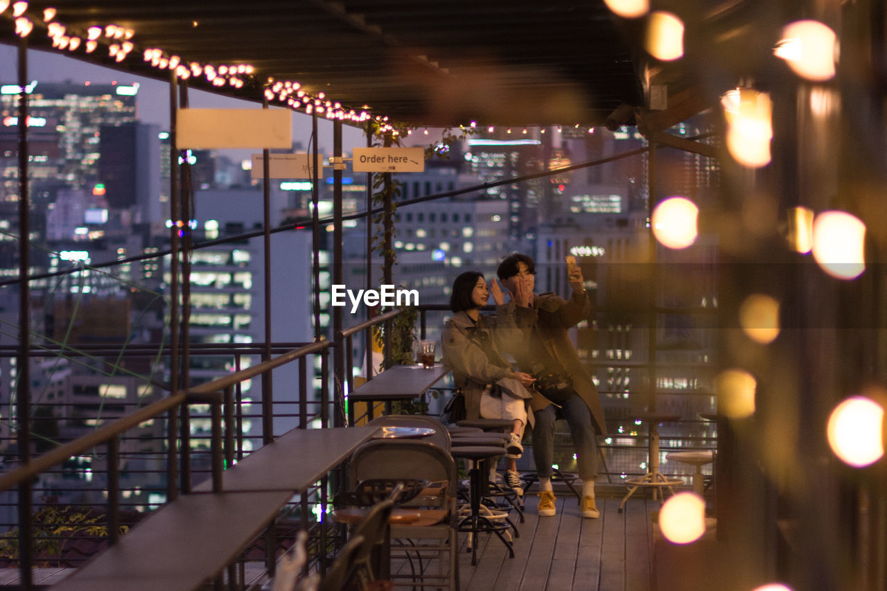 PEOPLE SITTING IN ILLUMINATED MODERN BUILDINGS AT NIGHT