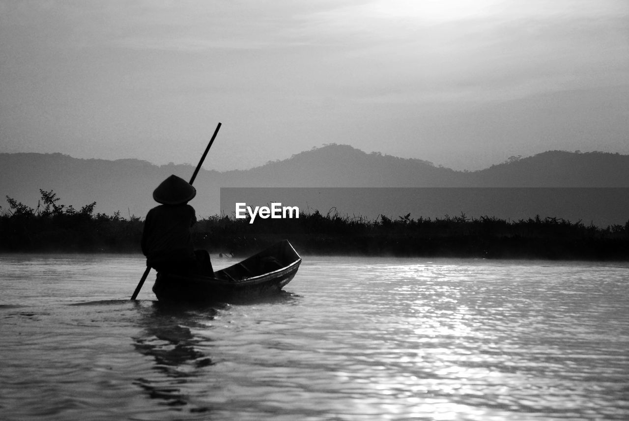 Man rowing boat in lake against sky