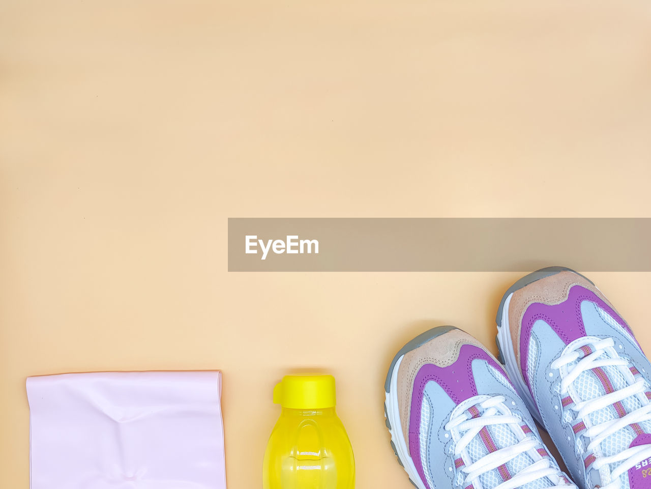 Set stylish sneakers, fitness rubber band stretch, yellow bottle on the beige background